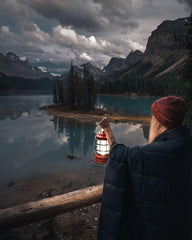 Barebones Forest Lantern red hanging on branch demonstrates versatile hanging options for cozy camp atmospheres.
