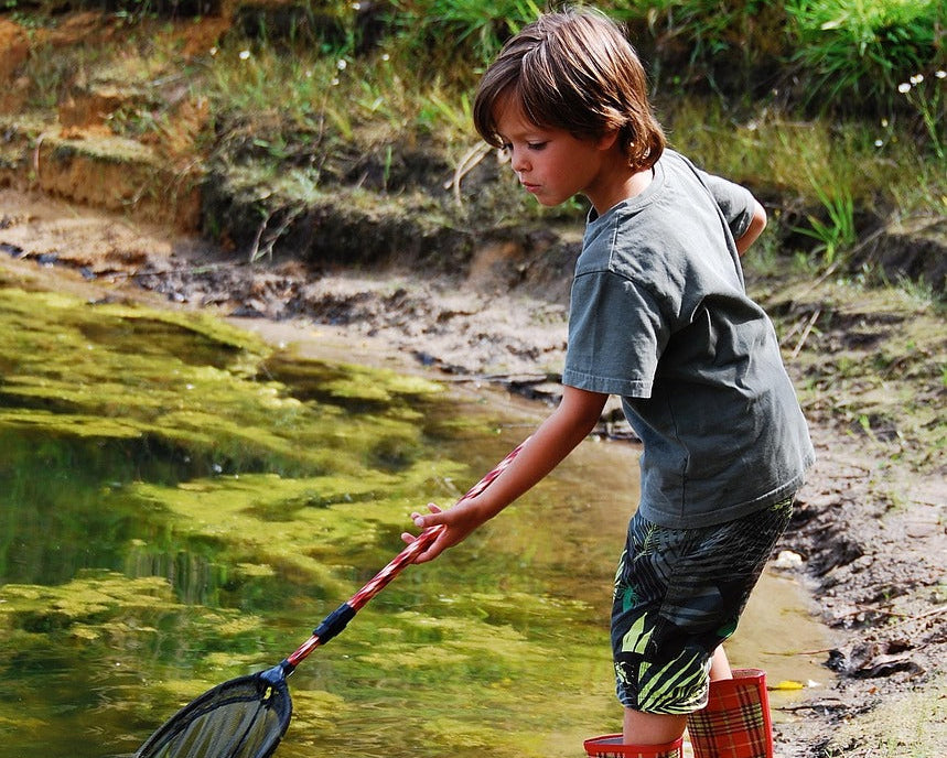 Young boy exploring nature by a forest lake with a fishing net representing Canada Wild outdoor adventure spirit.