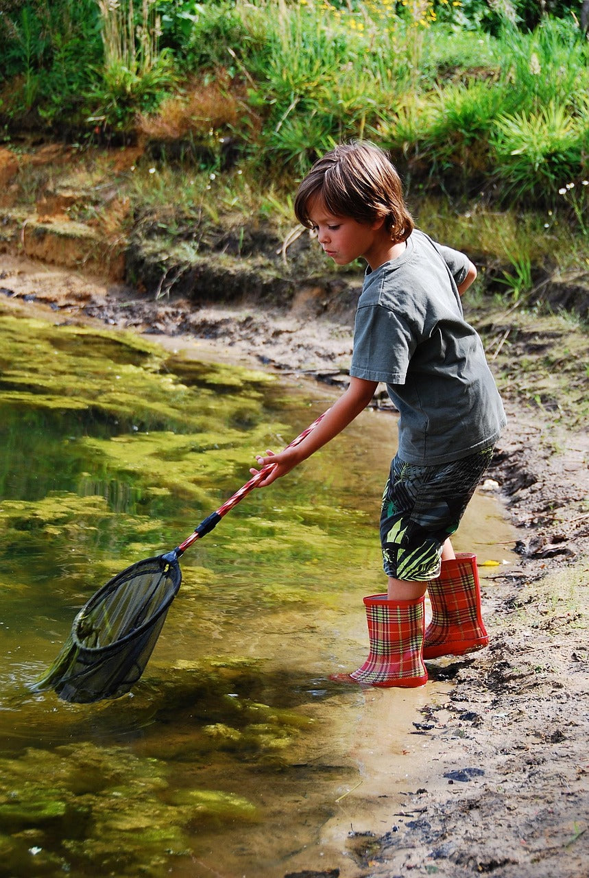 Young boy exploring nature by a forest lake with a fishing net representing Canada Wild outdoor adventure spirit.