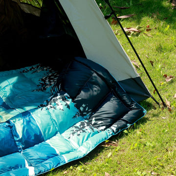 Hotkoko down camping blanket spread on campsite for warmth and comfort.