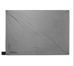 Matador Pocket Blanket 4.0 white stakes grounded on grass for windy stability.