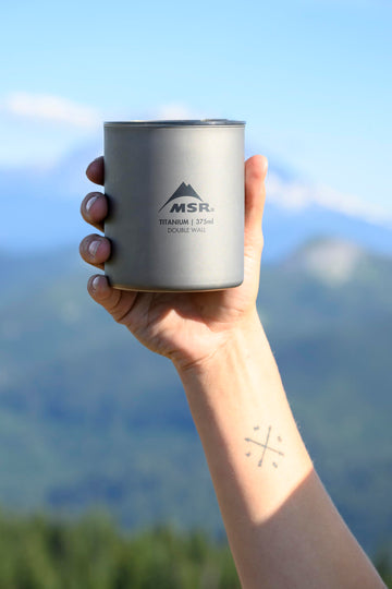 MSR Titan ultralight camp mug on campfire setup evokes backcountry coffee rituals.