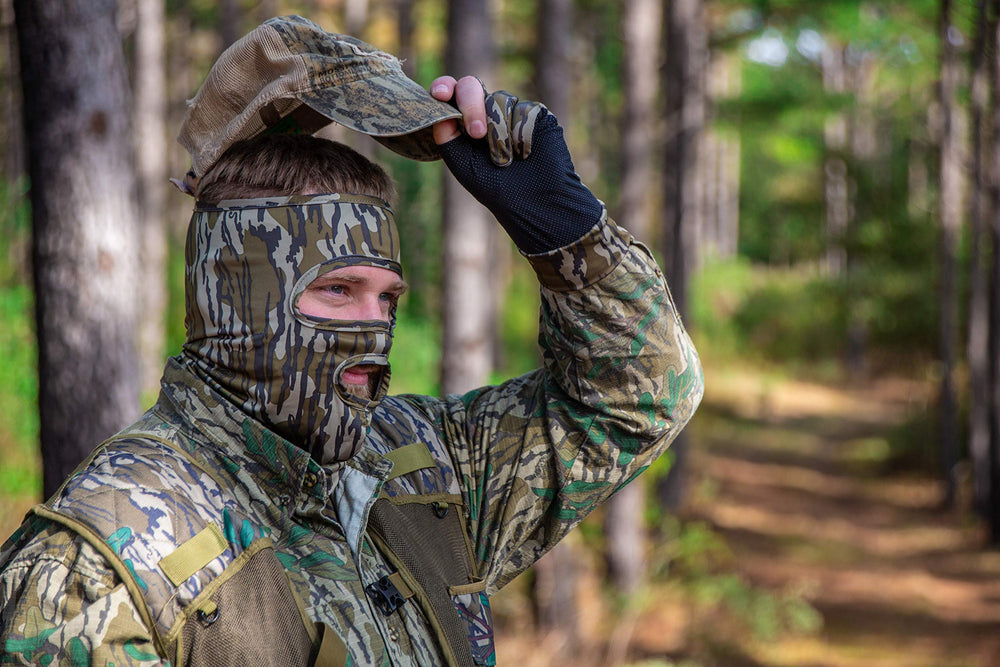 PRIMOS hunting mask in Real Tree camo blending into woodlands.