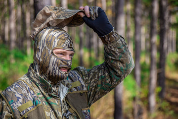 PRIMOS hunting mask in Real Tree camouflage enhances concealment in woodlands.