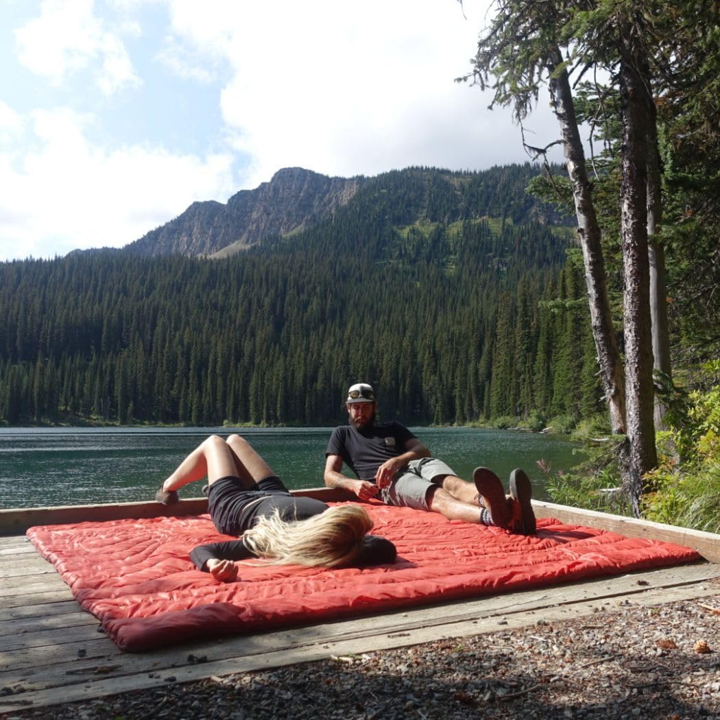 The Rumpl Original Puffy 2P blanket in deepwater color at a campsite.